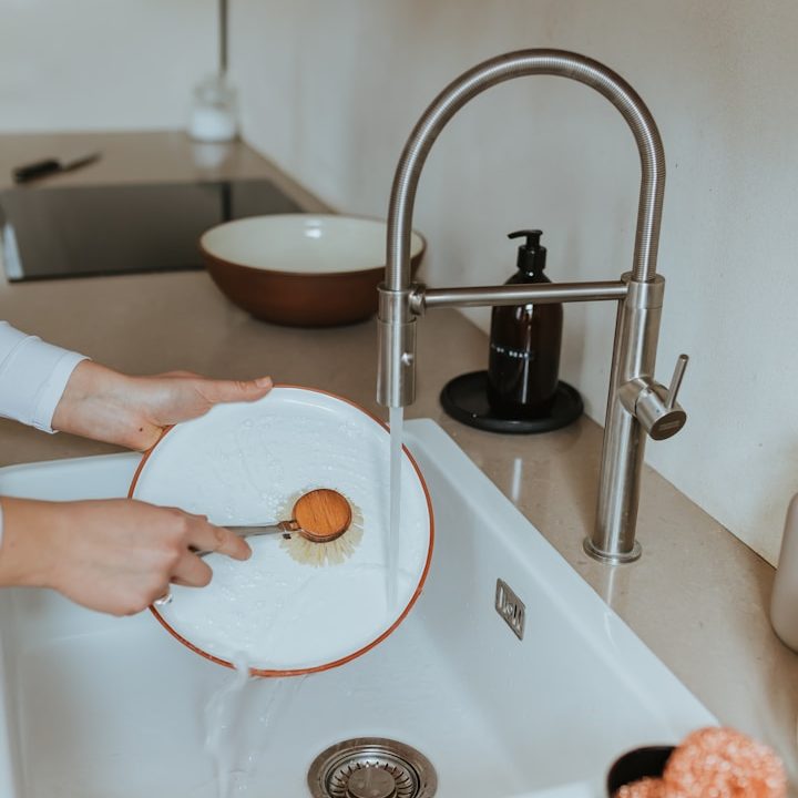 A person washing a plate with a sponge under a kitchen tap. Hot running water in a mobile kitchen trailer